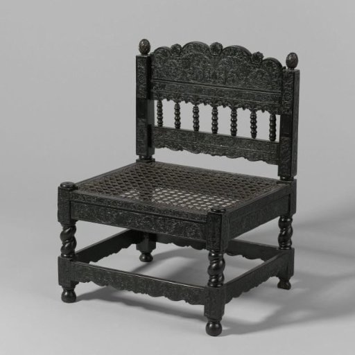 Chair of ebony with carved flower and leaf scrolls and a seat of woven reed