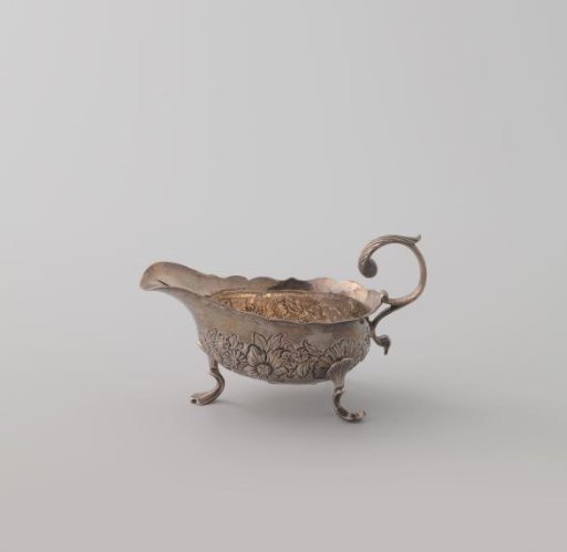 Silver cream jug on three curved feet with a spreading motif continued in the chased decoration on the body. Broad spout and S-shaped curved handle.