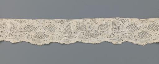 Strip of bobbin lace with symmetrical pattern with three-lobed cartouche and wave valley with half daisy and diagonal lines