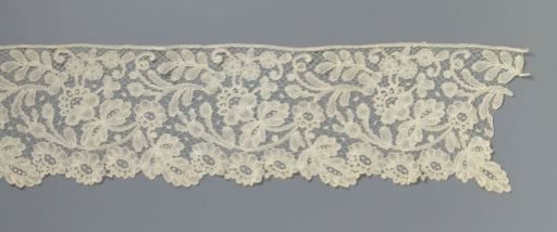 Strip of bobbin lace with three rosette flowers and a three-lobed leaf as a shell border