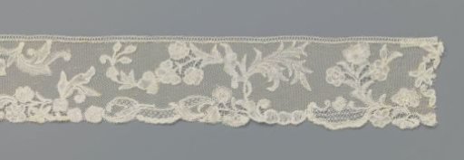 Strip of bobbin lace with flower and leaf motifs above a border with small flowers, volutes and elongated cartouches