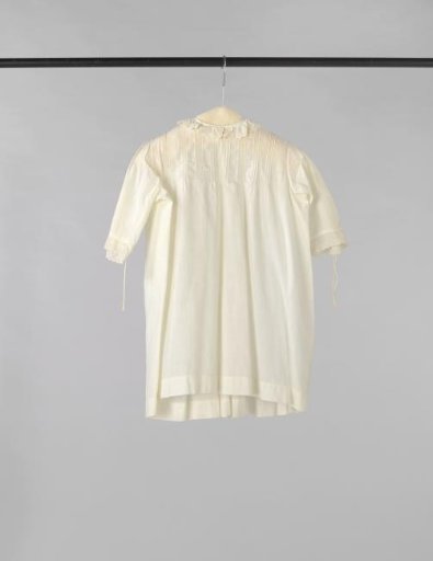 Children's pinafore of white cotton, decorated with inserts and strips of white embroidery and drawn work