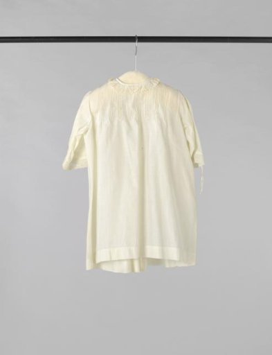Children's pinafore of white cotton, decorated with inserts and strips of white embroidery and drawn work
