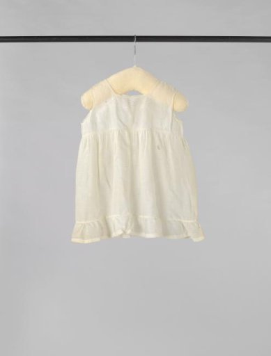 Sleeveless children's dress of white batiste (?), decorated with openwork borders, English embroidery, lace and a ruffle at the bottom