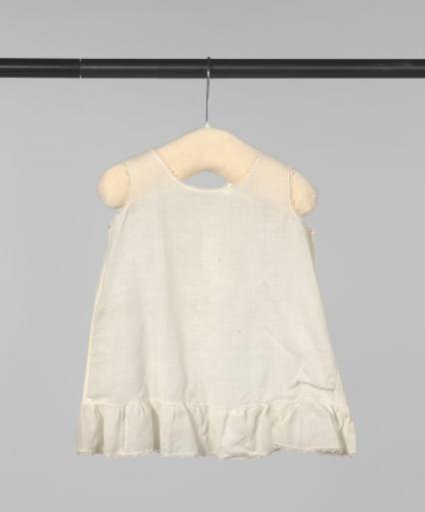 Sleeveless children's dress of white cotton (?), edged with a narrow openwork border and a ruffle at the bottom; back closure with three buttons