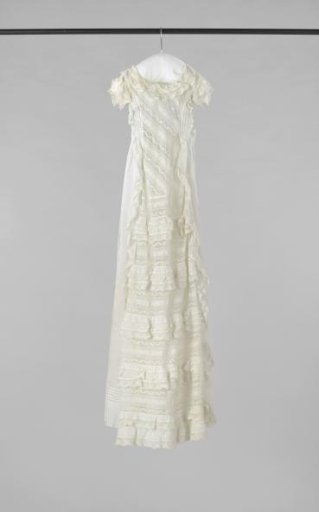 Christening gown of batiste with insertions of lace and whitework. Round neck and puffed sleeves, high waist. Wide band from side seams for bow on the back