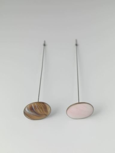 Hatpin of metal with a flat, oval head containing marbled pink/white glass