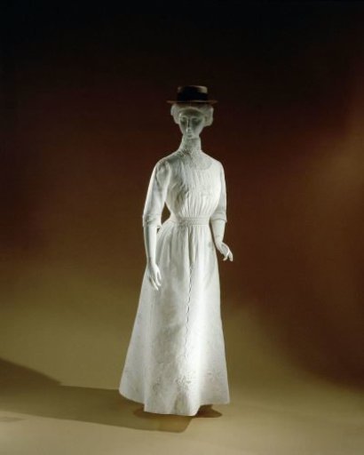 Tennis jacket with long sleeves and wide waistband, of transparent woven white cotton, decorated with stitched and open seams, white embroidered flower and leaf branches and lace.