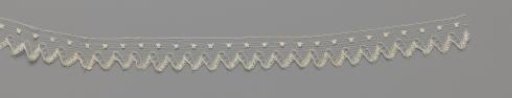 Strip of bobbin lace with zigzag border and one row of buttonholes in a blue tulle ground