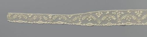 Band of needle lace with ovals on tops and in valleys of wavy leafy branch