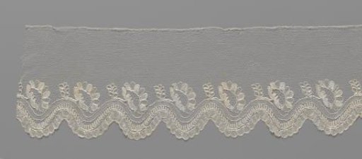 Strip of bobbin lace with wavy decorative band and obliquely placed oval flowers in the wave troughs