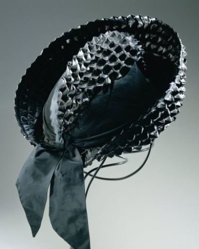 Hat of woven black raffia with flat crown and upturned brim at the front, decorated with a ribbon of black satin