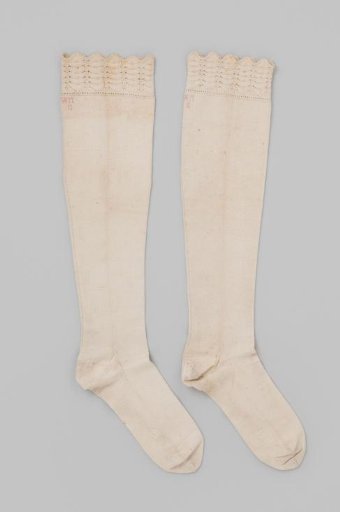 Stocking of plain white cotton tricot, with a border in openwork decorative stitch of rows of fan-shaped motifs and scalloped edge