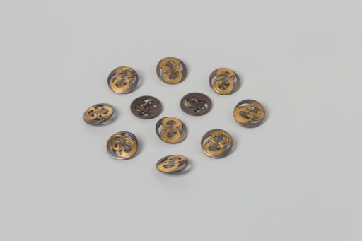 Button, flat and round, of metal partially painted with gold paint with a scroll motif, openwork and engraved