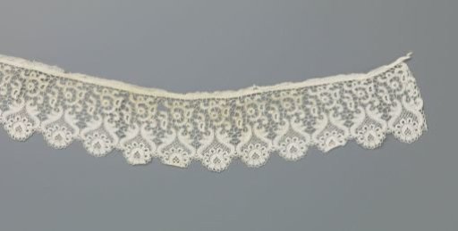Strip of machine lace with scalloped edge of round roses between mirrored S-shaped lines