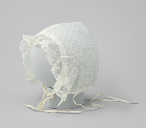 Baby cap of white textile with puffs on the front trimmed with a strip of scalloped lace and two bows