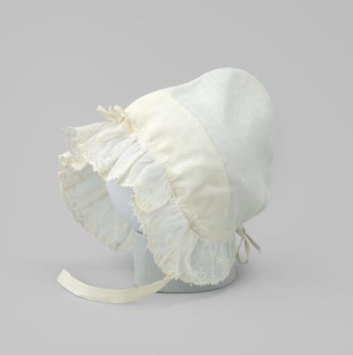 Baby bonnet of white fabric with gathered applied lightly scalloped strip of lace with picots