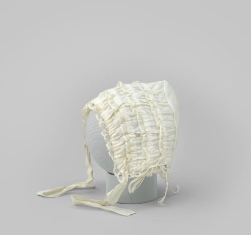 Baby cap of white textile with four ruffles trimmed with lightly scalloped picoted Valenciennes lace