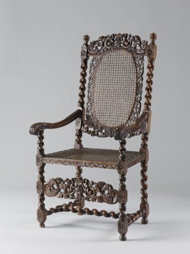 Armchair with caned seat; central splat openwork with putti holding a crown and acanthus scrolls. Vases on corner posts of the back