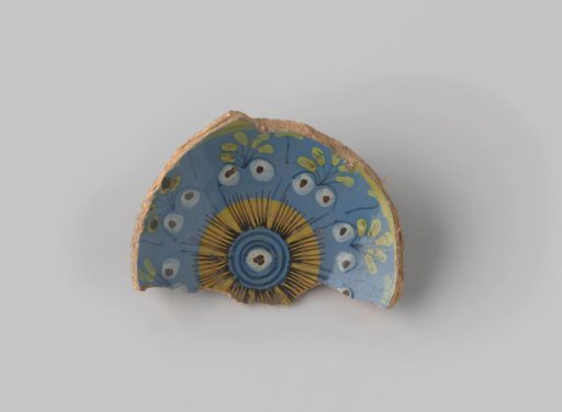Fragment of reddish-fired earthenware, with a foot ring, glazed blue on the front, with a painting of stylized floral forms in brown, blue, green, yellow and white on the flat