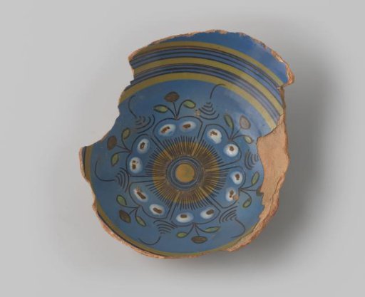 Fragment of yellow-fired earthenware, with footring, glazed blue on the front, with a painting of leaves and flowers in brown, blue, green, orange, yellow and white on the flat surface, surrounded by circles in brown and yellow