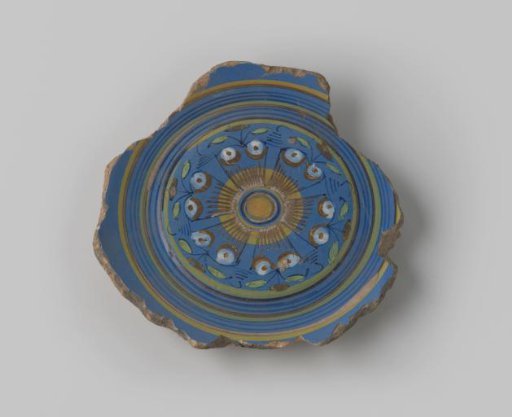 Fragment of yellow-fired earthenware, with footring, glazed blue on the front, with a painting of leaves and flowers in brown, blue, green, orange, yellow and white on the flat surface, surrounded by circles in brown and yellow