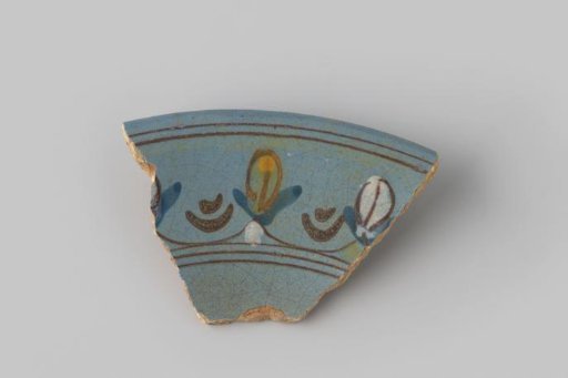 Fragment of white-fired earthenware, glazed blue on the front, with a painting of brown stripes with stylized flower forms in brown, blue, yellow and white between them
