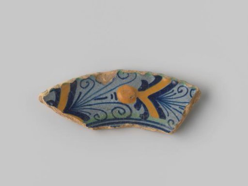 Plate fragment of yellow-fired earthenware, glazed blue on the upper side, with a painting of curls and stripes in green, blue and orange