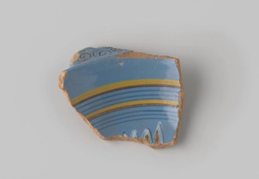 Fragment of red-firing earthenware, glazed on the upper side with blue glaze decorated with stripes, curls and petals in brown, yellow and white
