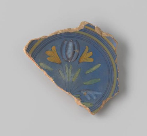 Sherd of reddish-baked earthenware, glazed blue on the upper side with a decoration of a scene of four flowers growing in the earth in brown, white, yellow, orange and green, and several circles in brown and yellow around them