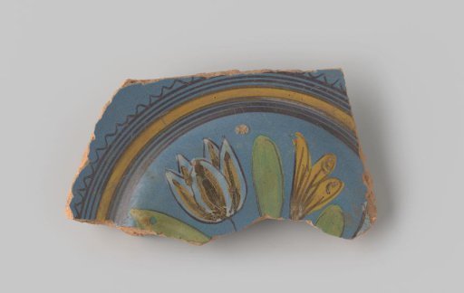Sherd of reddish-baked earthenware, glazed blue on the upper side with a decoration of a scene of two flowers growing in the earth in brown, white, yellow, orange and green, and several circles in brown and yellow around them