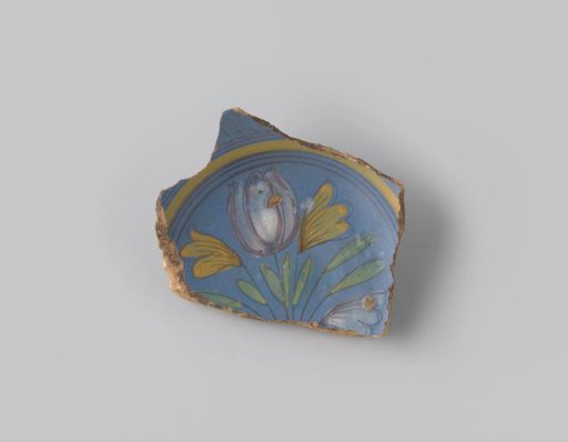 Sherd of reddish-baked earthenware, glazed blue on the upper side with a decoration of a scene of two flowers growing in the earth in brown, white, yellow, orange and green, and several circles in brown and yellow around them