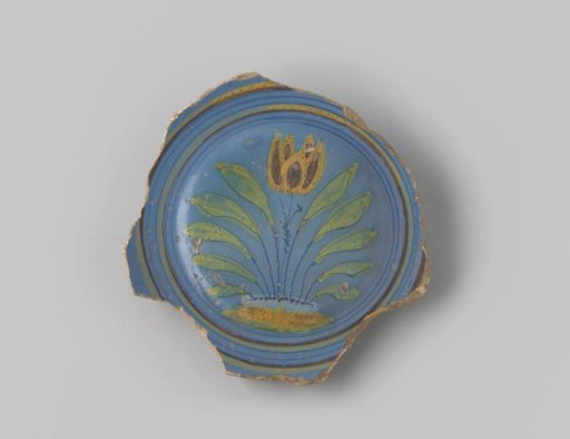 Sherd of reddish-baked earthenware, glazed blue on the upper side with a decoration of a scene of one tulip among leaves, growing in the earth in brown, white, yellow, orange and green, and several circles in brown, yellow and blue around them