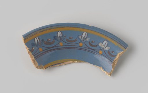 Fragment of reddish-fired earthenware, glazed blue on the upper side with a rim painted with semicircles and dots in yellow, brown, orange and white