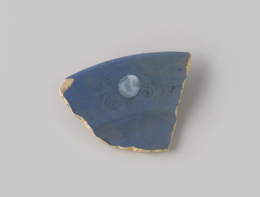 Fragment of whitish-fired earthenware, glazed blue on the upper side, decorated with a painting of a stylized flower form in brown, filled with white