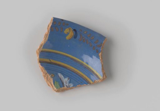 Fragment of red-fired earthenware, glazed blue on the upper side, decorated with a painting of a leafy vine, stripes and a part of a flower in brown, yellow, orange, white, blue and green
