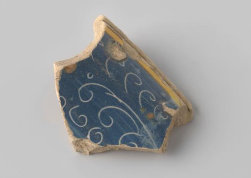 Fragment of reddish-fired earthenware, glazed blue on the upper side, with scratched curls and dots, and a yellow-glazed rim