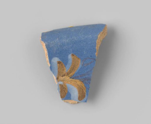 Fragment of reddish-fired earthenware, glazed blue on the upper side, with a portion of a leafy vine visible in brown, ochre and white