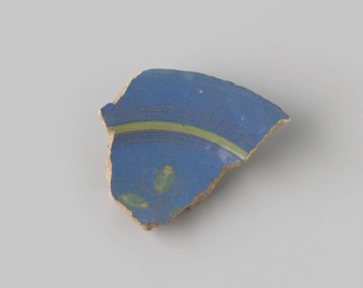 Fragment of reddish-fired earthenware, glazed blue on the upper side, with stripes and a wavy rim in brown and yellow, and on the flat a portion of a plant with two yellow leaves