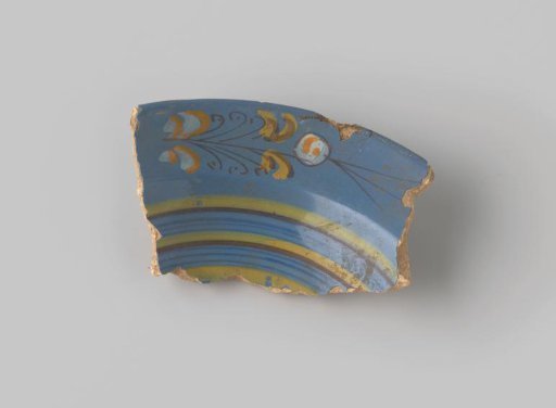 Fragment of red-fired earthenware, glazed blue on the front, with a painting of a flower in stylized form in brown, white, orange and yellow, and stripes in blue, brown and yellow