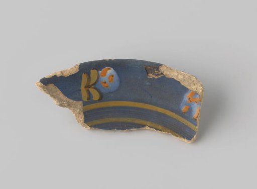 Fragment of yellowish-fired earthenware, glazed blue on the front, with a painted stylized floral form in yellow, brown, white and orange, and stripes in yellow and blue