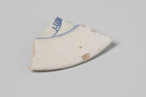 Sherd of a plate of earthenware with white tin glaze on the underside and white tin glaze on the upper side and a decoration in blue, damaged
