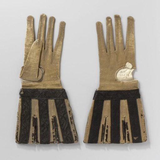 Glove of goat(?) leather, dyed ochre, with cut, loose tabs decorated with black satin ribbon embroidered with a floral pattern in black silk