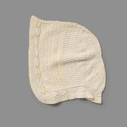 Knitted cap of white cotton with a finely pleated border, next to border with strung leaf motif and further decorated with a smaller leaf motif in borders