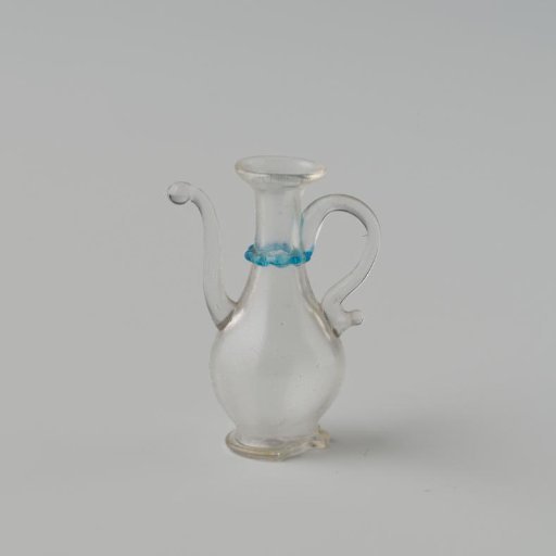Jug of clear colourless glass, smooth slender model on a flat slightly outward curved base; blue pinched neck ring, S-shaped solid spout and handle.
