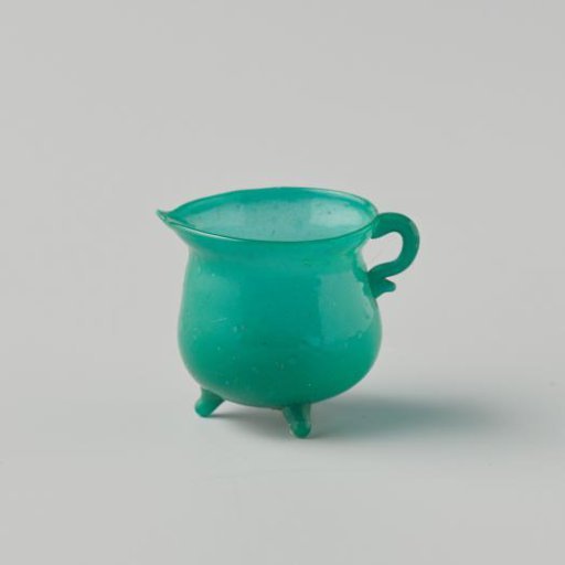 Cooking jug of opaque green glass (probably imitation green earthenware); on three feet, with spout and handle.