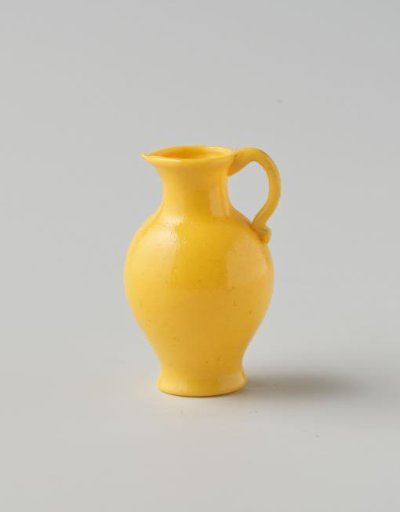 Jug of opaque yellow glass (probably imitation yellow earthenware); round and slender model with spout, applied handle and indented base.