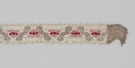 Ribbon of silk brocade; on a white ground is a silver-colored zigzag pattern with red and pink flowers between them
