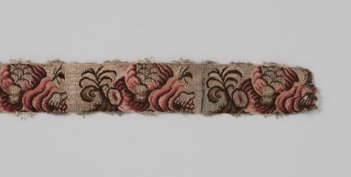 Belt ribbon of silk brocade; on a silver-colored ground is a repeating pattern in dark red, pink and brown in the shape of a snail shell (?) from which fruit and leaves emerge