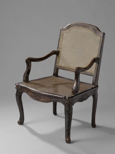 Armchair of light brown lacquered beechwood with diagonally placed S-shaped legs, seat and back of woven rush, seat rails, front legs and top rail with leaf ornament